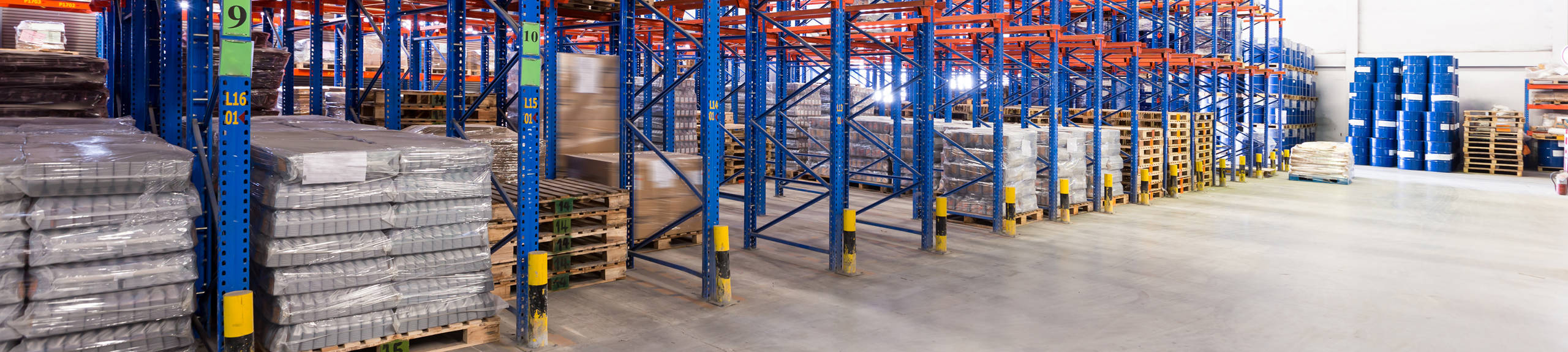 The inside of a warehouse with a concrete floor and rows of industrial-sized shelving.