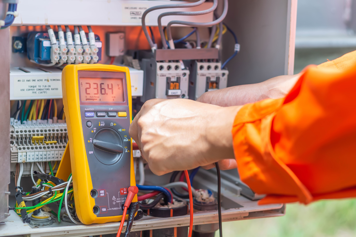 A test engineer wearing an orange uniform using a specialist device to test machinery.