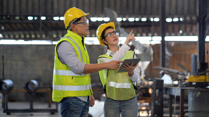 Two engineering specialists in high visibility gear and hard hats talking on a factory floor.