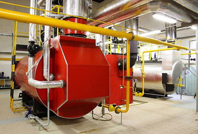 A large red industrial pressure vessel, indoors with multiple pipes connected to the machine.