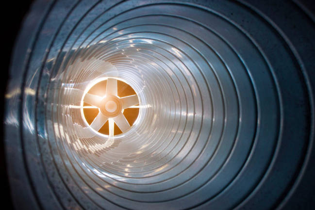Inside view of an industrial ventilation pipe with a large steel fan at the end.