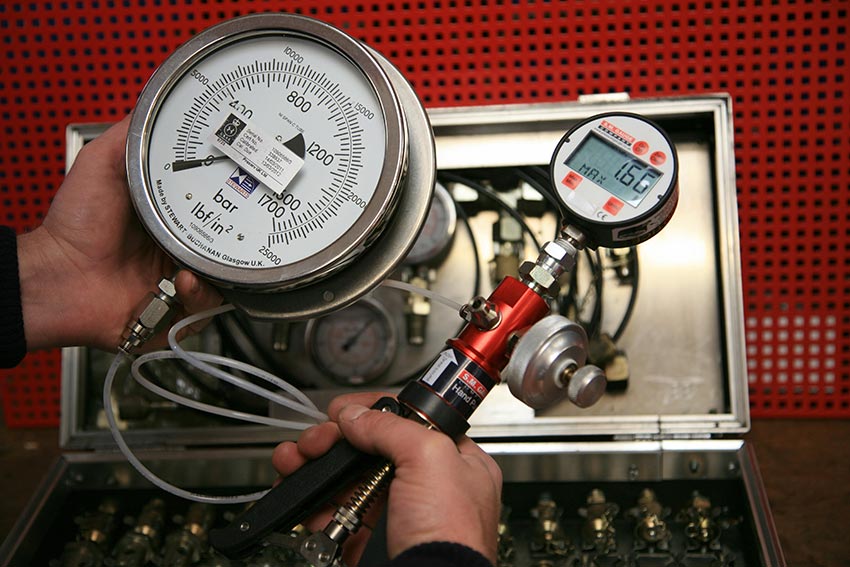 Inspector holding a device with a large gauge used for hydrostatic pressure testing.