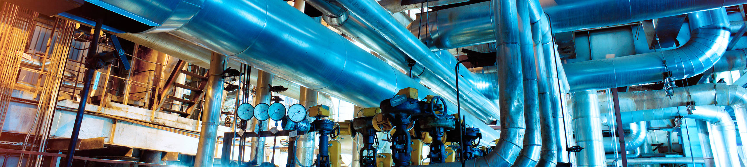 Machinery with large metal pipes and multiple pressure gauges inside of an industrial plant.